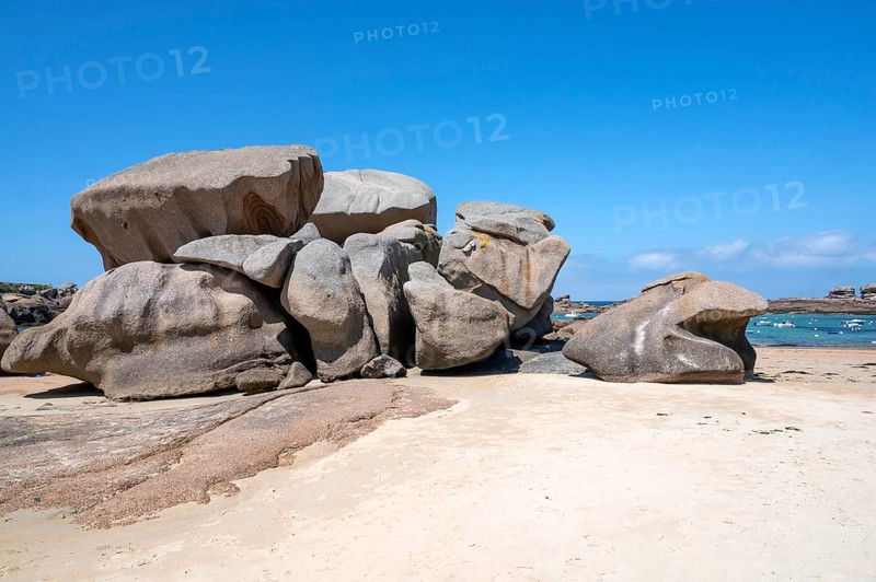 Spectacular pink granite rocks, sculpted by wind and sea, pile up on the beach of the Cote de Granit Rose, while the clear, turquoise-blue water reveals seaweed and light-coloured sand on the seabed at low tide, Tregastel, Cotes-d'Armor department, Brittany region, France