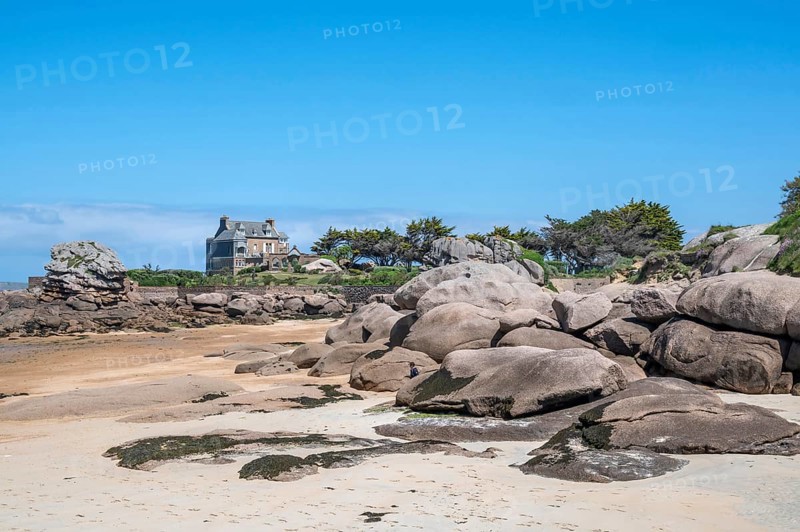 View from the harbour beach of Trégastel on the Côte de Granit Rose at low tide over the iconic pink granite rocks to a typical Breton house with granite façade and slate roof, Tregastel, Cotes-d'Armor department, Brittany region, France