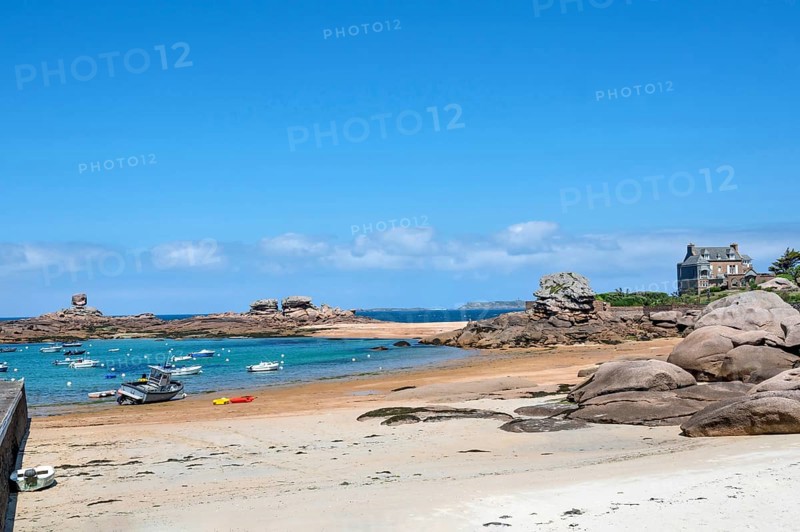 On the harbour beach of Tregastel on the Cote de Granit Rose, small sailing boats lie on the light sand at low tide against the backdrop of the iconic pink granite rocks and Breton houses, Tregastel, Cotes-d'Armor department, Brittany region, France