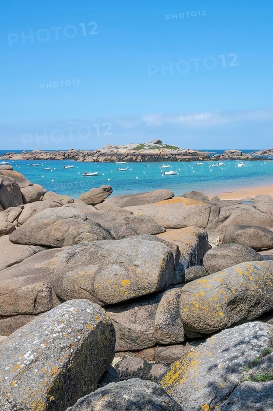 The wide bay of Tregastel on the Cote de Granit Rose shows the turquoise blue sea with white sailing boats and the characteristic round pink granite rocks, framed by large boulders in the foreground, Tregastel, Cotes-d'Armor department, Brittany region, France