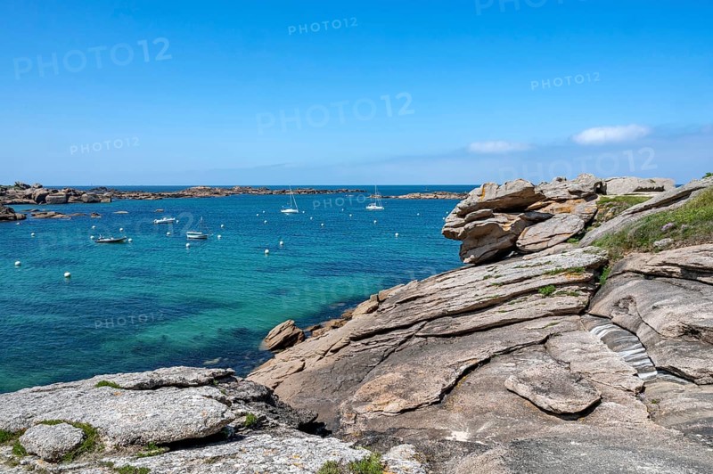 View from the GR 34 coastal hiking trail of the extensive sandy beach of the Plage de la Greve Blanche on the Cote de Granit Rose with anchored boats and buoys, framed by the characteristic rounded pink granite rocks, Tregastel, Cote-d'Armor department, Brittany region, France