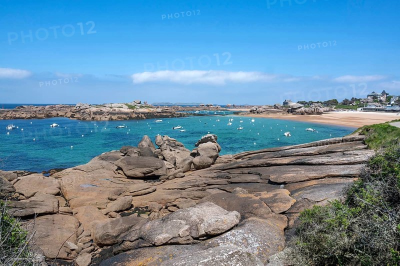 View from the GR 34 coastal hiking trail of the extensive sandy beach of the Plage de la Greve Rose on the Cote de Granit Rose with anchored boats and buoys, framed by the characteristic rounded pink granite rocks, Tregastel, Cote-d'Armor department, Brittany region, France