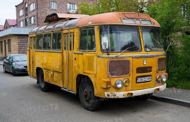 An old yellow bus stands abandoned on the street in an urban environment, clear signs of use, PAZ-672, minibus of the Soviet manufacturer Pavlovsky, Armenia