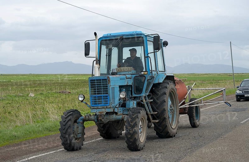 A blue tractor is driven by a man on a country road with fields and cloudy sky, Belarus MTZ-82 tractor or MTS-82, Armenia