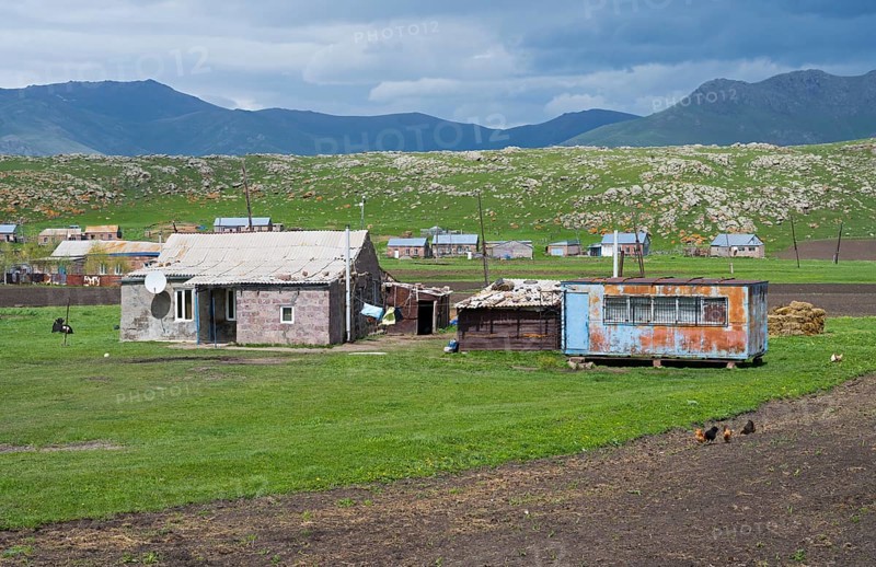Rustic barns and buildings on green pasture against a mountainous backdrop with clouds in the sky, Shenkani village, Aragazotn province, Armenia