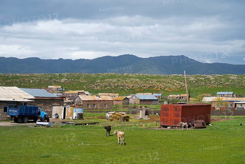 Rural settlement with huts and animals on a green pasture surrounded by mountains under a cloudy sky, Shenkani village, Aragazotn province, Armenia