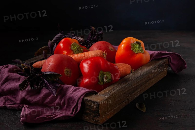 Peppers, tomatoes, carrots lie in a wooden box dark photo