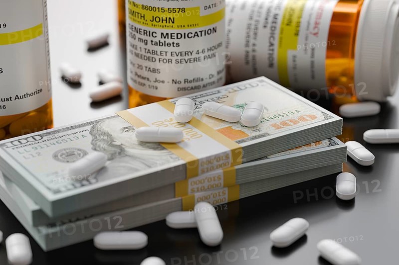 Prescription medicine bottles and pills next to stacks of 100 dollar bills