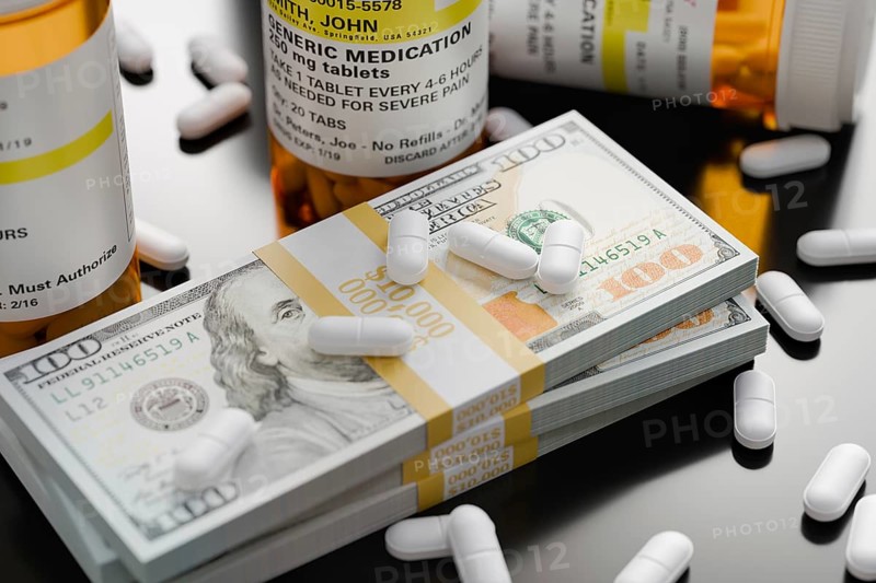 Prescription medicine bottles and pills next to stacks of 100 dollar bills