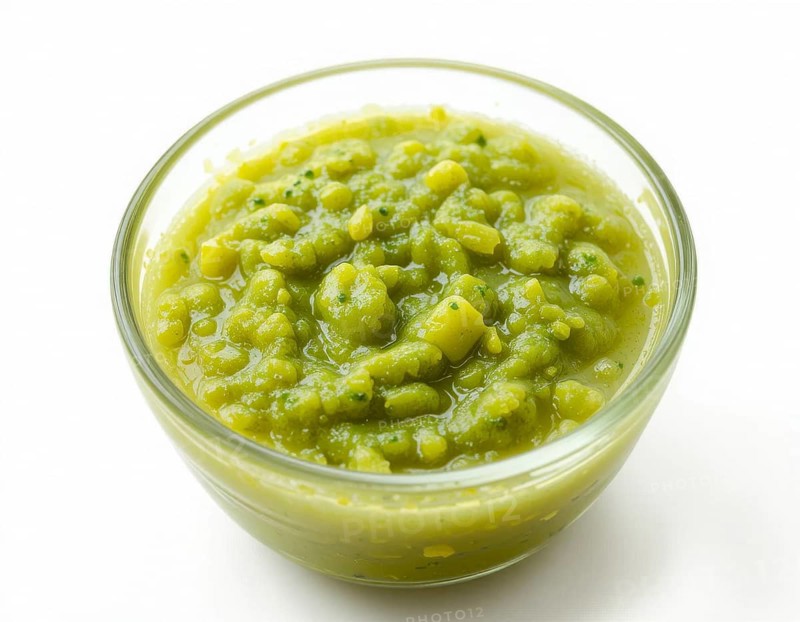 A clear glass bowl holds a thick, textured pea soup, showcasing a fresh, healthy meal. The bright green color pops against the clean white backdrop, AI generated