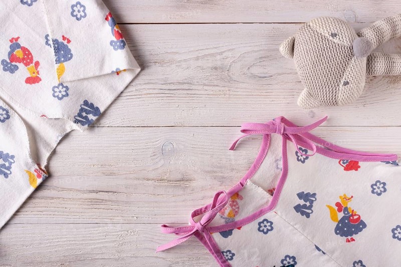 Clothes for a newborn and a rattle on a white wooden background