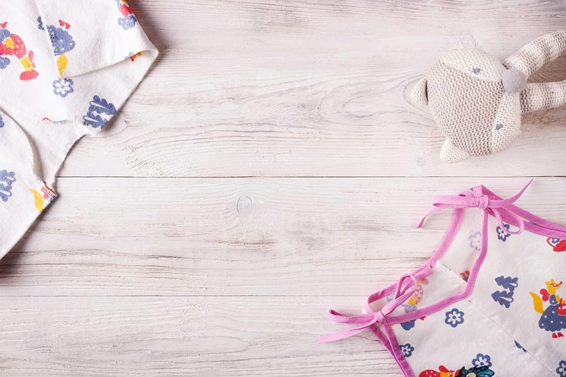 Clothes for a newborn and a rattle on a white wooden background