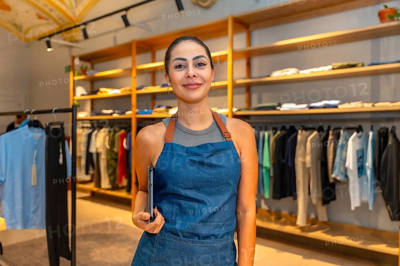 Portrait of a young saleswoman smiling and holding a tablet, working in a modern clothing store, ready to assist customers