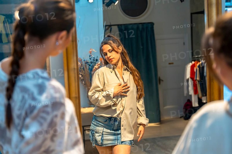 Young woman trying on new clothes, looking at her reflection in a mirror in a store dressing room