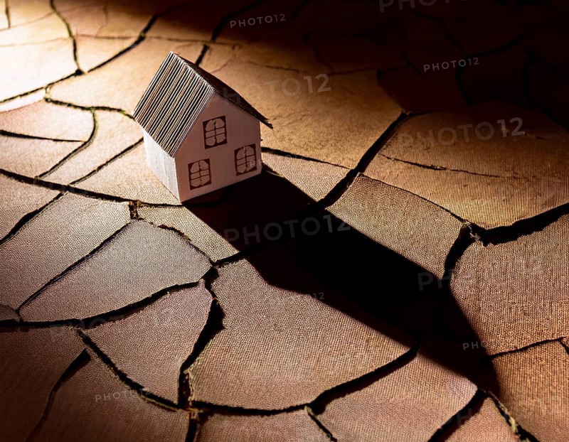 A cardboard miniature house placed on cracked, dry soil, illustrating drought, environmental impact, or harsh climatic conditions. An expression of vulnerability and adaptation amidst ecological challenges, AI generated