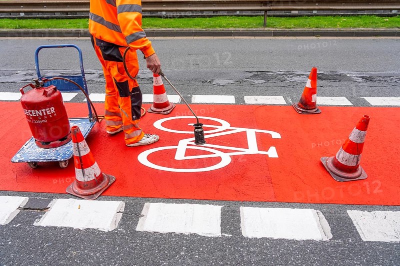 Application of red road surfacing on a cycle lane, inner-city road, so-called cold plastic surfacing, in the colour traffic red, RAL3020, the coloured marking is intended to attract more attention from motorists for cyclists, on cycle paths along roads and at junctions, roundabouts, Essen, North Rhine-Westphalia, Germany