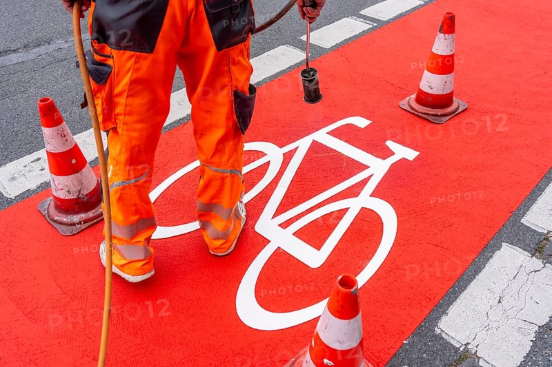 Application of red road surfacing on a cycle lane, inner-city road, so-called cold plastic surfacing, in the colour traffic red, RAL3020, the coloured marking is intended to attract more attention from motorists for cyclists, on cycle paths along roads and at junctions, roundabouts, Essen, North Rhine-Westphalia, Germany