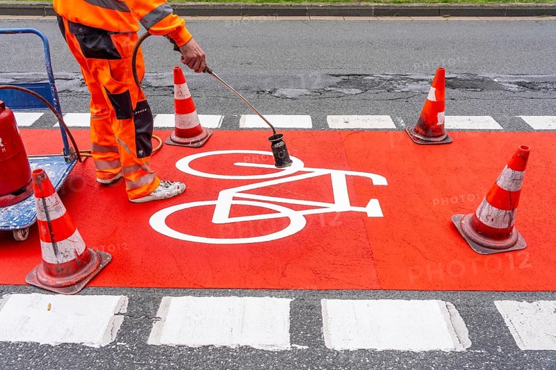Application of red road surfacing on a cycle lane, inner-city road, so-called cold plastic surfacing, in the colour traffic red, RAL3020, the coloured marking is intended to attract more attention from motorists for cyclists, on cycle paths along roads and at junctions, roundabouts, Essen, North Rhine-Westphalia, Germany