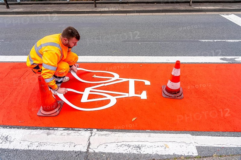 Application of red road surfacing on a cycle lane, inner-city road, so-called cold plastic surfacing, in the colour traffic red, RAL3020, the coloured marking is intended to attract more attention from motorists for cyclists, on cycle paths along roads and at junctions, roundabouts, Essen, North Rhine-Westphalia, Germany
