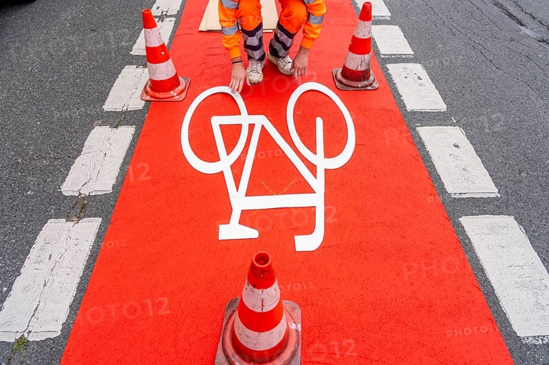 Application of red road surfacing on a cycle lane, inner-city road, so-called cold plastic surfacing, in the colour traffic red, RAL3020, the coloured marking is intended to attract more attention from motorists for cyclists, on cycle paths along roads and at junctions, roundabouts, Essen, North Rhine-Westphalia, Germany
