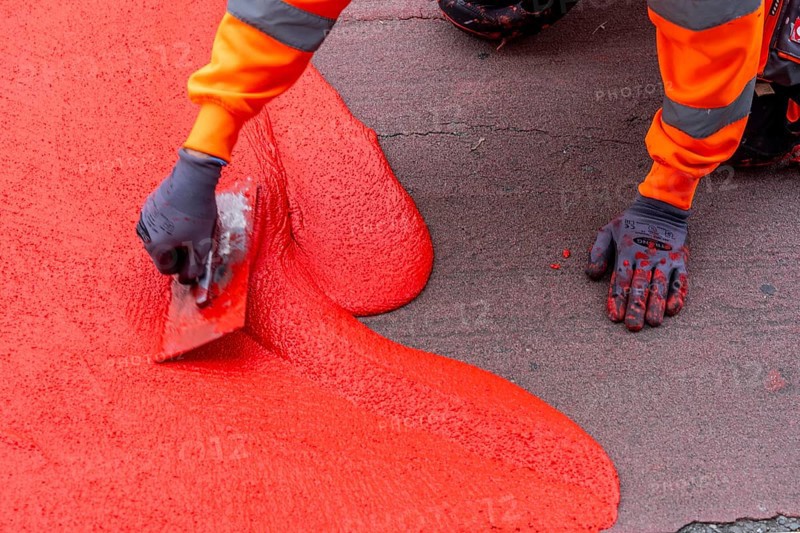 Application of red road surfacing on a cycle lane, inner-city road, so-called cold plastic surfacing, in the colour traffic red, RAL3020, the coloured marking is intended to attract more attention from motorists for cyclists, on cycle paths along roads and at junctions, roundabouts, Essen, North Rhine-Westphalia, Germany