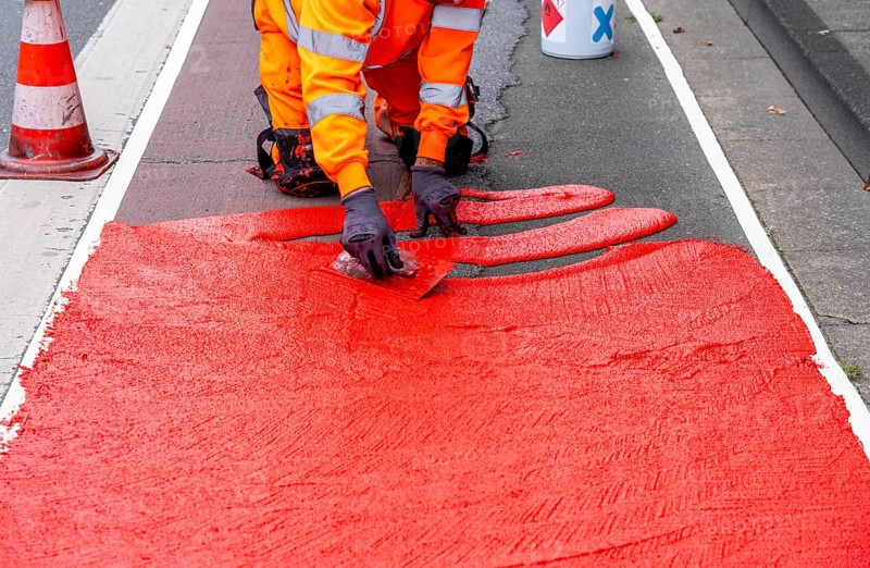 Application of red road surfacing on a cycle lane, inner-city road, so-called cold plastic surfacing, in the colour traffic red, RAL3020, the coloured marking is intended to attract more attention from motorists for cyclists, on cycle paths along roads and at junctions, roundabouts, Essen, North Rhine-Westphalia, Germany