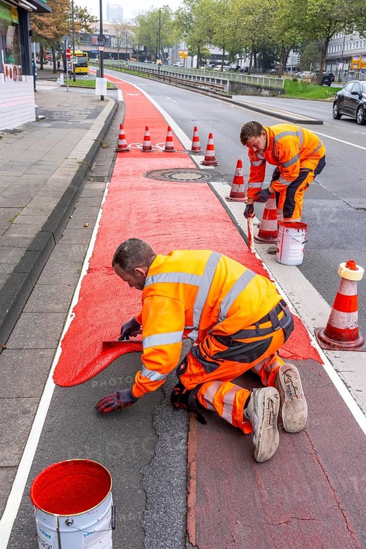 Application of red road surfacing on a cycle lane, inner-city road, so-called cold plastic surfacing, in the colour traffic red, RAL3020, the coloured marking is intended to attract more attention from motorists for cyclists, on cycle paths along roads and at junctions, roundabouts, Essen, North Rhine-Westphalia, Germany