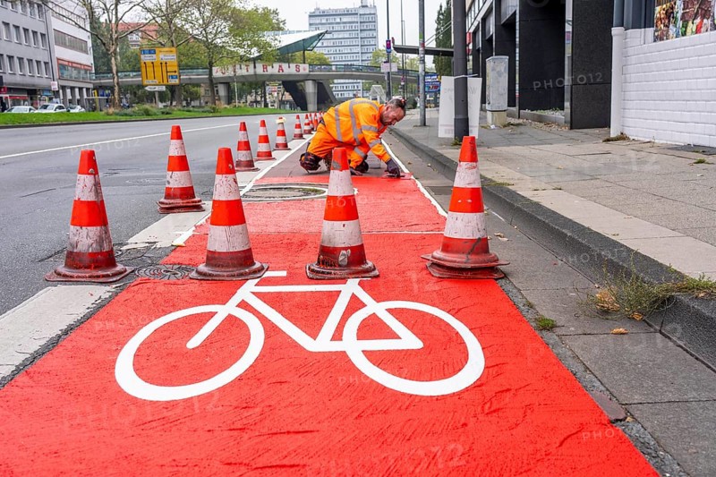 Application of red road surfacing on a cycle lane, inner-city road, so-called cold plastic surfacing, in the colour traffic red, RAL3020, the coloured marking is intended to attract more attention from motorists for cyclists, on cycle paths along roads and at junctions, roundabouts, Essen, North Rhine-Westphalia, Germany