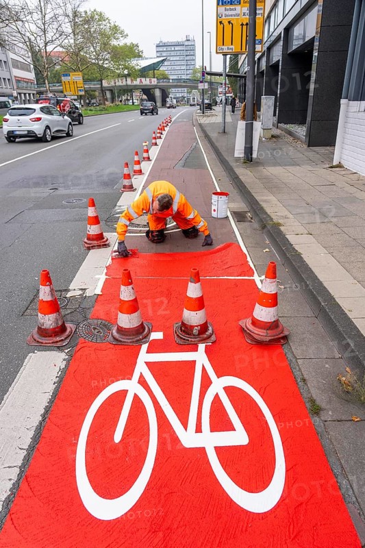 Application of red road surfacing on a cycle lane, inner-city road, so-called cold plastic surfacing, in the colour traffic red, RAL3020, the coloured marking is intended to attract more attention from motorists for cyclists, on cycle paths along roads and at junctions, roundabouts, Essen, North Rhine-Westphalia, Germany