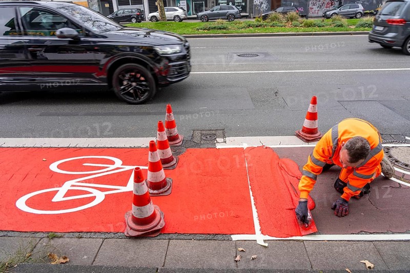 Application of red road surfacing on a cycle lane, inner-city road, so-called cold plastic surfacing, in the colour traffic red, RAL3020, the coloured marking is intended to attract more attention from motorists for cyclists, on cycle paths along roads and at junctions, roundabouts, Essen, North Rhine-Westphalia, Germany