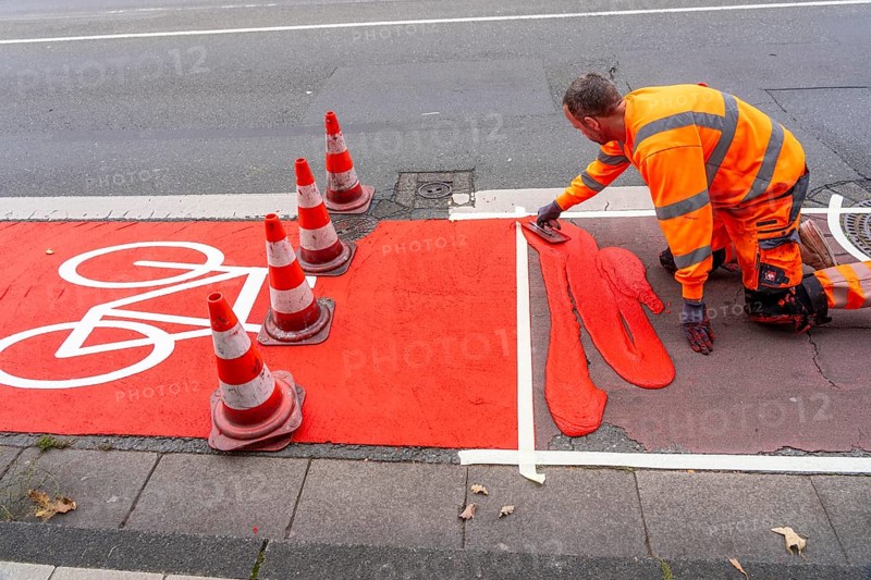 Application of red road surfacing on a cycle lane, inner-city road, so-called cold plastic surfacing, in the colour traffic red, RAL3020, the coloured marking is intended to attract more attention from motorists for cyclists, on cycle paths along roads and at junctions, roundabouts, Essen, North Rhine-Westphalia, Germany