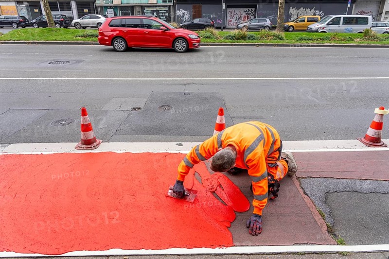 Application of red road surfacing on a cycle lane, inner-city road, so-called cold plastic surfacing, in the colour traffic red, RAL3020, the coloured marking is intended to attract more attention from motorists for cyclists, on cycle paths along roads and at junctions, roundabouts, Essen, North Rhine-Westphalia, Germany