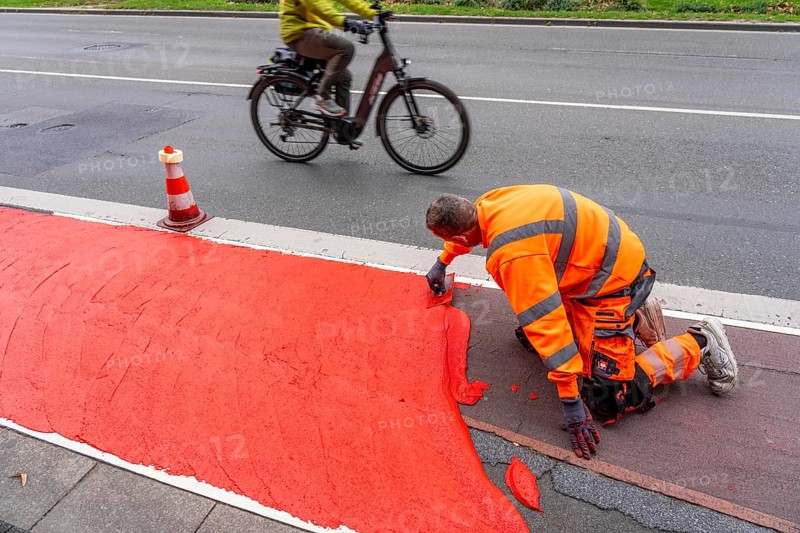 Application of red road surfacing on a cycle lane, inner-city road, so-called cold plastic surfacing, in the colour traffic red, RAL3020, the coloured marking is intended to attract more attention from motorists for cyclists, on cycle paths along roads and at junctions, roundabouts, Essen, North Rhine-Westphalia, Germany
