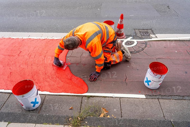 Application of red road surfacing on a cycle lane, inner-city road, so-called cold plastic surfacing, in the colour traffic red, RAL3020, the coloured marking is intended to attract more attention from motorists for cyclists, on cycle paths along roads and at junctions, roundabouts, Essen, North Rhine-Westphalia, Germany