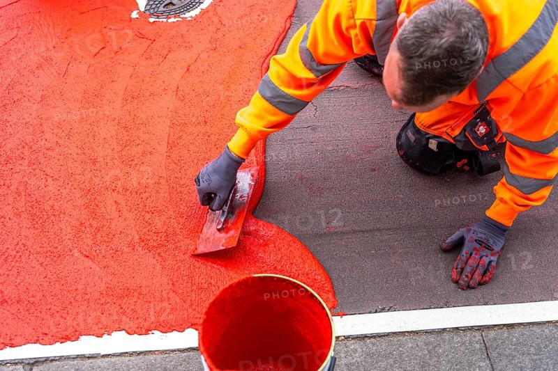 Application of red road surfacing on a cycle lane, inner-city road, so-called cold plastic surfacing, in the colour traffic red, RAL3020, the coloured marking is intended to attract more attention from motorists for cyclists, on cycle paths along roads and at junctions, roundabouts, Essen, North Rhine-Westphalia, Germany