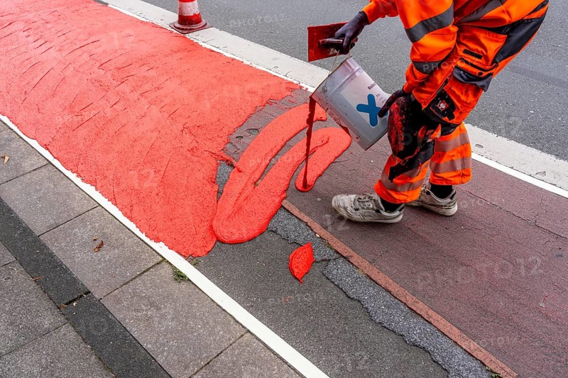 Application of red road surfacing on a cycle lane, inner-city road, so-called cold plastic surfacing, in the colour traffic red, RAL3020, the coloured marking is intended to attract more attention from motorists for cyclists, on cycle paths along roads and at junctions, roundabouts, Essen, North Rhine-Westphalia, Germany