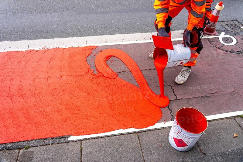 Application of red road surfacing on a cycle lane, inner-city road, so-called cold plastic surfacing, in the colour traffic red, RAL3020, the coloured marking is intended to attract more attention from motorists for cyclists, on cycle paths along roads and at junctions, roundabouts, Essen, North Rhine-Westphalia, Germany
