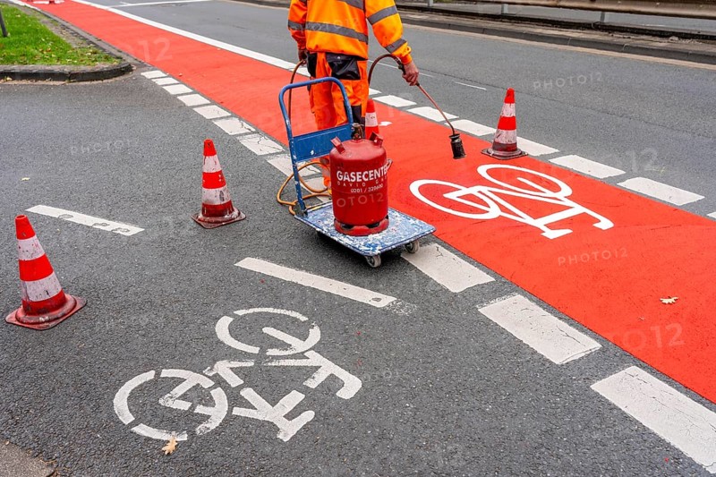 Application of red road surfacing on a cycle lane, inner-city road, so-called cold plastic surfacing, in the colour traffic red, RAL3020, the coloured marking is intended to attract more attention from motorists for cyclists, on cycle paths along roads and at junctions, roundabouts, Essen, North Rhine-Westphalia, Germany