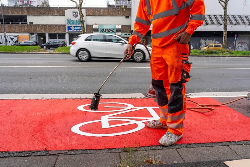 Application of red road surfacing on a cycle lane, inner-city road, so-called cold plastic surfacing, in the colour traffic red, RAL3020, the coloured marking is intended to attract more attention from motorists for cyclists, on cycle paths along roads and at junctions, roundabouts, Essen, North Rhine-Westphalia, Germany