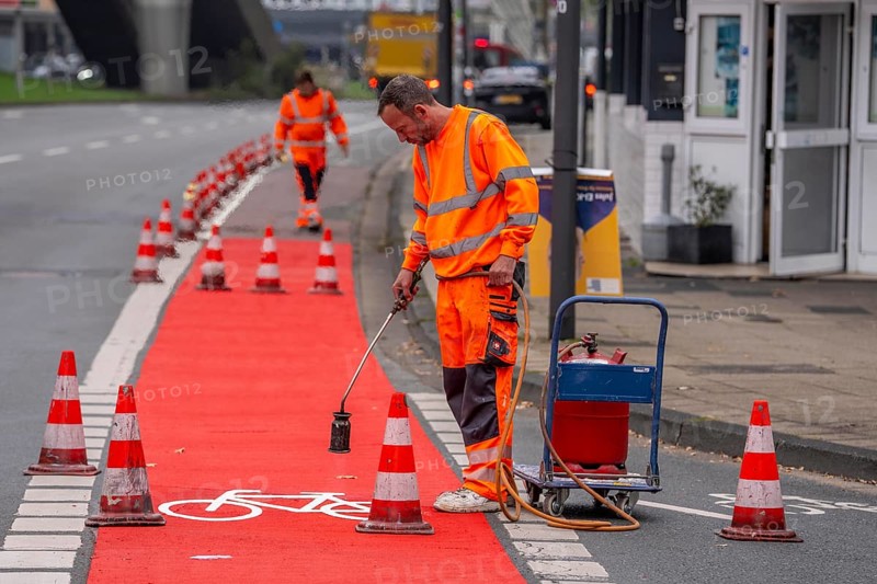 Application of red road surfacing on a cycle lane, inner-city road, so-called cold plastic surfacing, in the colour traffic red, RAL3020, the coloured marking is intended to attract more attention from motorists for cyclists, on cycle paths along roads and at junctions, roundabouts, Essen, North Rhine-Westphalia, Germany