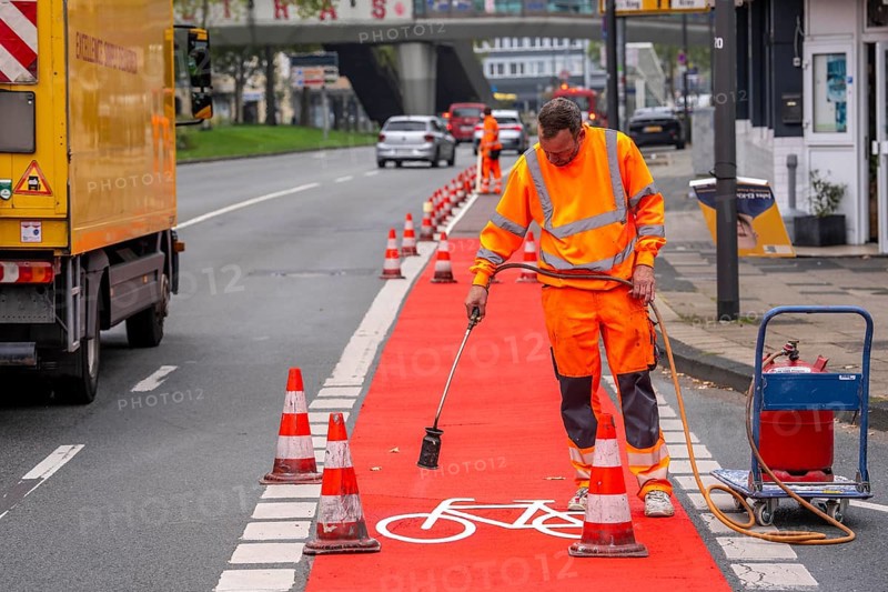 Application of red road surfacing on a cycle lane, inner-city road, so-called cold plastic surfacing, in the colour traffic red, RAL3020, the coloured marking is intended to attract more attention from motorists for cyclists, on cycle paths along roads and at junctions, roundabouts, Essen, North Rhine-Westphalia, Germany