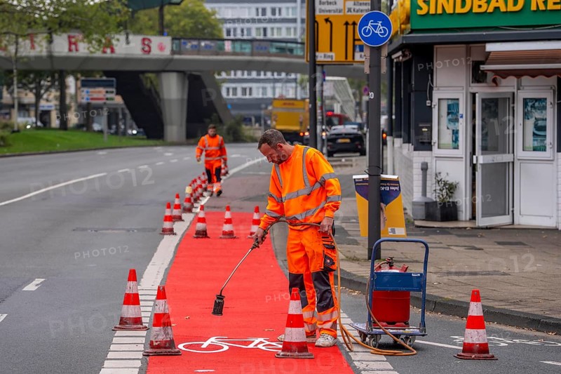 Application of red road surfacing on a cycle lane, inner-city road, so-called cold plastic surfacing, in the colour traffic red, RAL3020, the coloured marking is intended to attract more attention from motorists for cyclists, on cycle paths along roads and at junctions, roundabouts, Essen, North Rhine-Westphalia, Germany