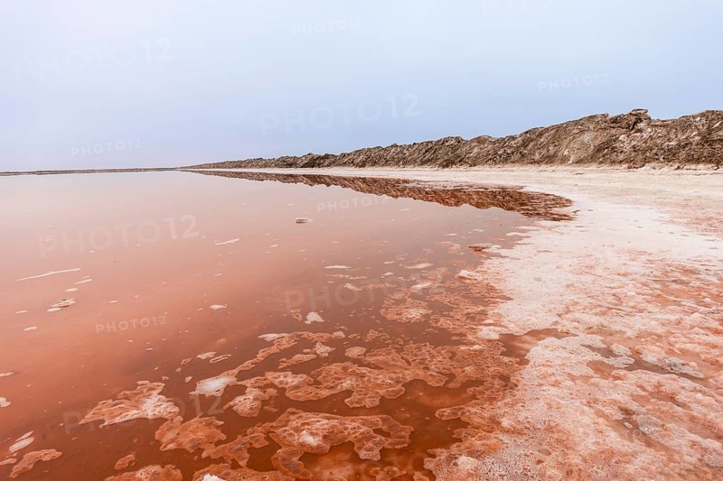 Pink salt flats with mineral-rich water in Sandwich Harbour, Namib-Naukluft National Park, Namibia. Rugged desert landscape with unique colors and textures, permit required to visit