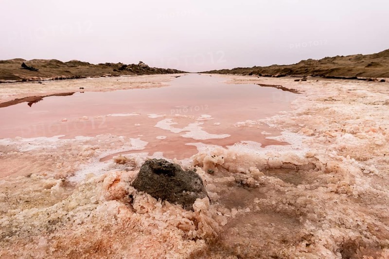 Pink salt flats with mineral-rich water in Sandwich Harbour, Namib-Naukluft National Park, Namibia. Rugged desert landscape with unique colors and textures, permit required to visit