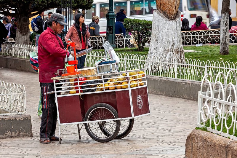A street vendor operates a fruit stand on a pavement in a busy city, selling fresh juice in the city of Potosi in Bolivia