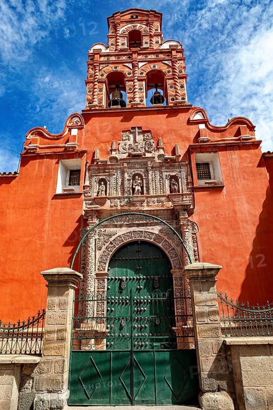 Door of a colonial building with red façade and bell tower under a clear blue sky, The churches of the city of Potosi in Bolivia