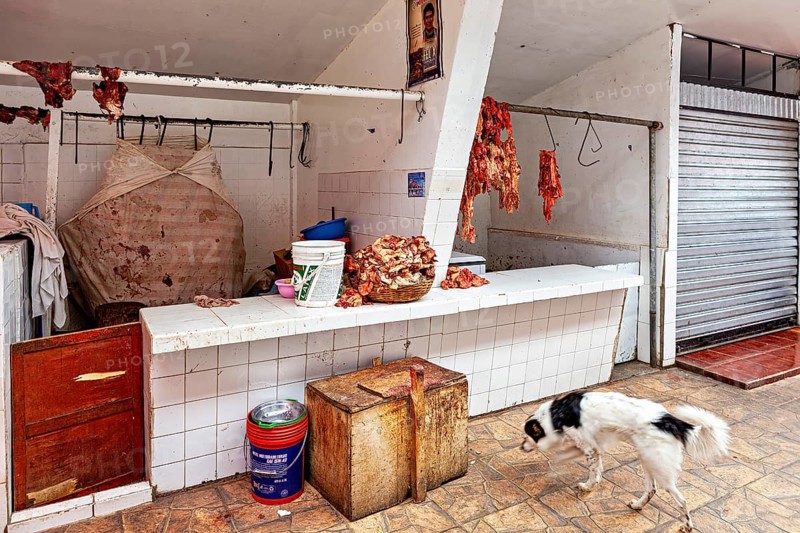 A dog walks past a table of raw meat and closed stalls, The meat market in the market halls of Potosi in Bolivia