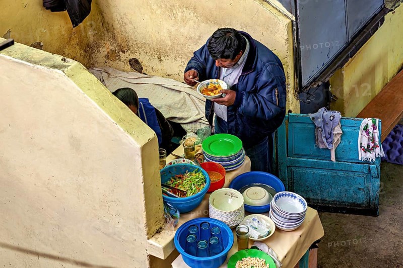 A man eats in a cosy corner with colourful crockery and a laid table, A man eats at a market stall in the market halls of Potosi Bolivia