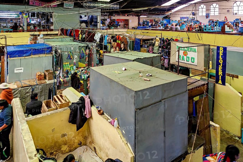 Lively market hall with numerous stalls and people in colourful clothing. Signs show various shops, inside the market halls of Potosi Bolivia