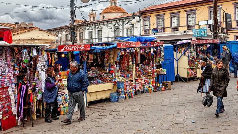 Colourful market stalls with Coca-Cola signs on a busy pavement full of people, Small market stalls in the centre of Potosi in Bolivia